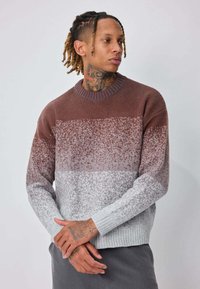 Pull en tricot présentant un dégradé de couleurs marron, gris et blanc, avec un col et des poignets côtelés, ainsi qu'un motif texturé moucheté.