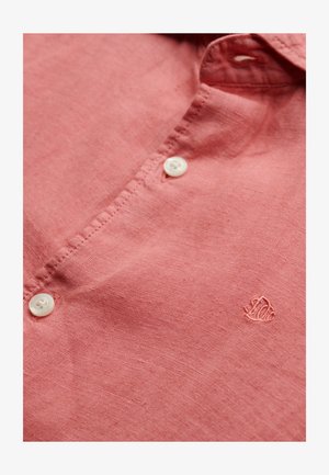 Koszulka lniana w kolorze koralowym z szerokim kołnierzykiem, z białymi guzikami oraz subtelnym haftem logo, prezentująca miękką strukturę i lekką, oddychającą tkaninę.