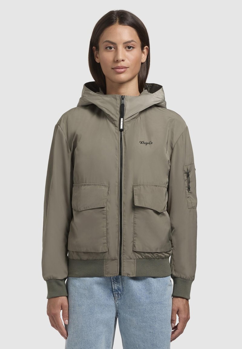 Veste bomber légère couleur vert olive avec capuche, fermeture éclair, deux poches avant et poignets côtelés. Texture lisse et design minimaliste.