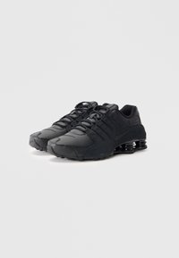 Sapatos de desporto pretos com um upper texturizado, apresentando atacadores, um colarinho acolchoado e uma distinta entressola Shox preta para maior amortecimento.