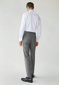 Witte button-up shirt, grijze broek met een gladde afwerking en zwarte nette schoenen. Casual look met minimale details op het shirt en de broek.