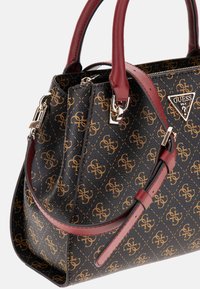Black handbag with gold logo pattern, burgundy handles, and silver hardware accents. Features a structured design and top zip closure.