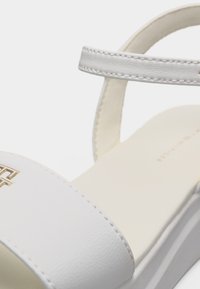 Λευκό δερμάτινο σανδάλι με λουράκι στον αστράγαλο, ανοιχτή μύτη και χρυσή λεπτομέρεια λογότυπου στο μπροστινό λουράκι.