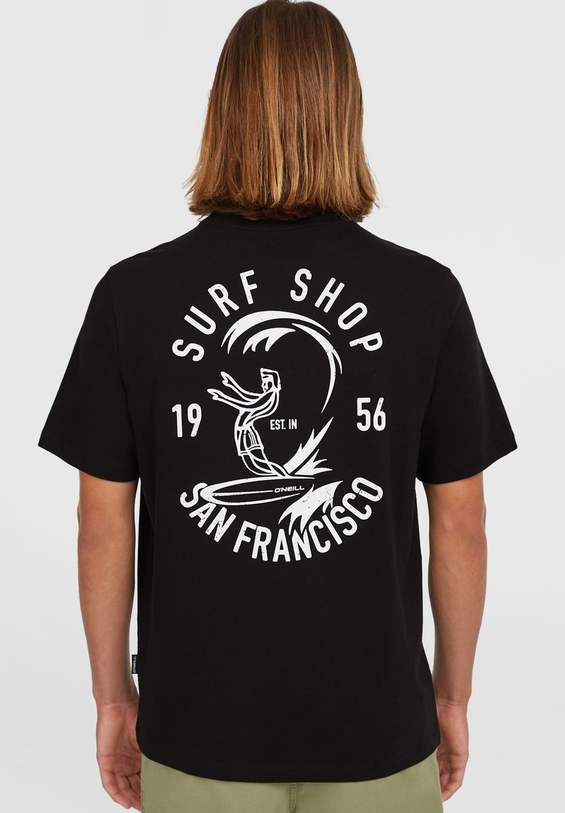 Fekete pamut póló, fehér grafikával, amely tartalmazza a "Surf Shop" feliratot, egy szörföst egy hullámban, valamint a "San Francisco" feliratot és az "1956" évet.