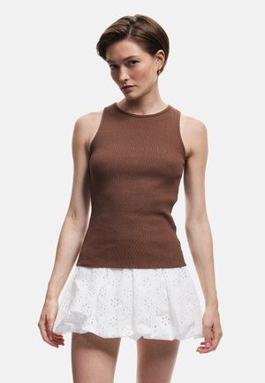 Top sin mangas de canalé marrón con un cuello alto, combinado con una falda blanca con bordados florales y un silueta acampanada.