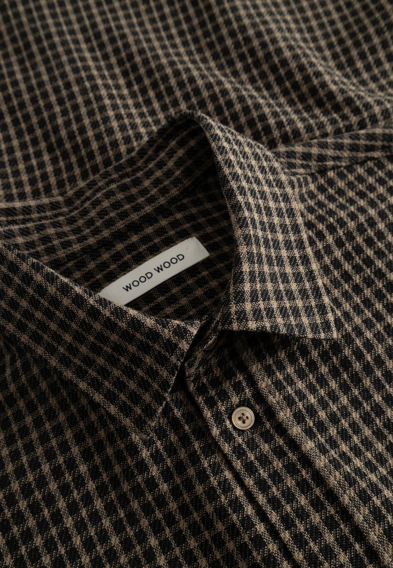 Camicia con colletto caratterizzata da un motivo a quadri nero e marrone, tessuto morbido, con un'etichetta che recita "WOOD WOOD" e un singolo dettaglio con bottone beige.