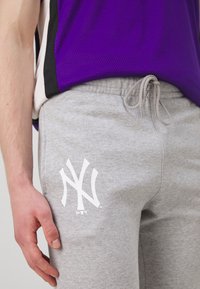 Sive tajice s elastičnim pojasom i vezicom. Sadrži bijeli logotip New York Yankeesa na butini. Mekana, ležerna tekstura tkanine.