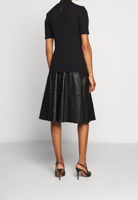 Czarny prążkowany top z krótkimi rękawami, z wysokim kołnierzem i zamkiem z tyłu. Połączony z lejącą się czarną skórzaną spódnicą midi oraz sandałami na obcasach.