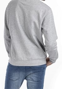 Felpa grigia dal taglio comodo, con collo tondo e bordo a costine, abbinata a jeans di denim blu con dettagli sulle tasche posteriori.