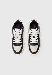 Zapatillas negras y crema con un patrón texturizado y secciones suaves. Presentan cordones blancos y un interior de marca en rojo.