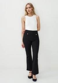 Zwarte flared pants met voorzakken en goudkleurige knopen, gecombineerd met een witte mouwloze top. Glad materiaal met een aansluitende taille.