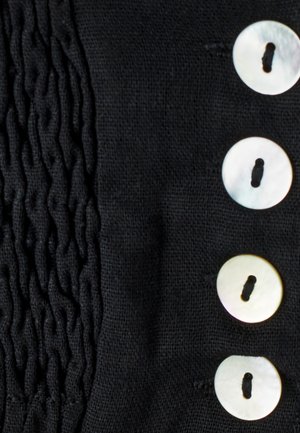 Juoda medžiaga, kairėje turi tekstūruotą, raukšlėtą skyrių, dešinėje – keturis apvalius, šviesą atspindinčius mygtukus.