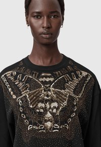 Sudadera negra con un diseño intrincado de mariposas de lentejuelas doradas y detalles a lo largo del escote. Tela suave con un corte relajado.