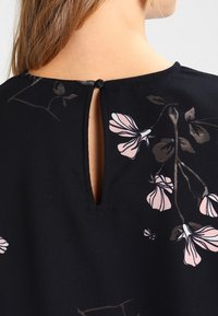 Top in tessuto nero con scollatura a chiave sulla schiena e chiusura con bottone, decorato con motivi floreali rosa e sottili accenti marroni.