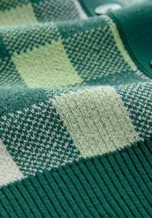 Material tricotat cu un model de carouri verzi și verde deschis; texturat cu un tiv cu nervuri în partea de jos; nasturi vizibili pe margine.