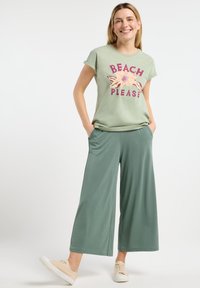 T-shirt vert clair avec un graphique "BEACH PLEASE" en rose et beige, assorti à un pantalon vert large et décontracté. Style décontracté, en coton.