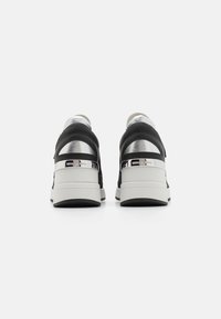 Sorte og sølv sneakers med en tekstureret bag, glatte detaljer, en klodset hvid sål og metallisk branding på hælen.