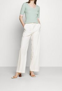 Haut vert clair côtelé à manches courtes avec des accents roses, associé à un pantalon blanc à jambes larges et des sandales à talons beiges.