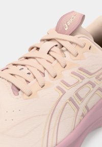 Helle rosa Sportschuh mit strukturiertem Stoff, runder Zehenform, kontrastierenden Schnürsenkeln und einem lila Akzent auf der Zunge. Verfügt über ein Logo und Designdetails.