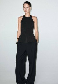 Black peplum top with halter neck design paired with loose-fit black trousers. Smooth texture, minimal seams, and subtle tailoring details.