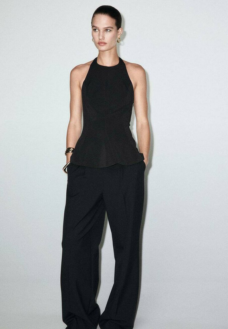 Black peplum top with halter neck design paired with loose-fit black trousers. Smooth texture, minimal seams, and subtle tailoring details.