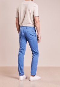 Ljusblå lätta chinos, slim fit, tillverkade av en blandning av bomull. Har subtila fickdetaljer, bärs med en beige t-shirt och vita sneakers.