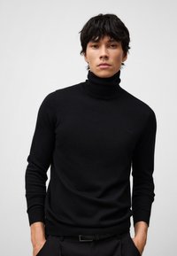 Czarny sweter z golfem wykonany z miękkiego materiału, z długimi rękawami i dopasowanym krojem. Minimalne detale z logo na klatce piersiowej.