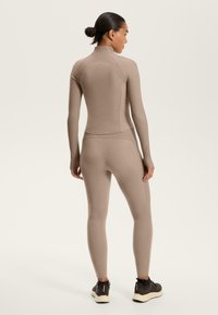 Beige Activewear-Set, bestehend aus einem langärmeligen Oberteil und Leggings. Strukturierter Rippstoff mit hohem Kragen und nahtloser Verarbeitung.