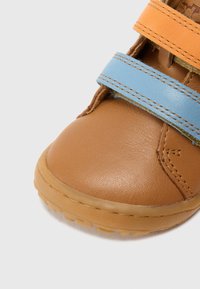 Pantof maro din piele cu curele din material albastru și portocaliu; vârf rotunjit și talpă de cauciuc texturată; detalii vizibile de cusătură și căptușeală interioară moale.