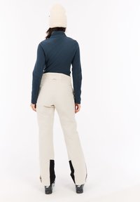 Lichtbeige skibroek met een hoge taille, gecombineerd met een donkerblauwe langärmige top. Zwarte accenten bij de broekzomen. Gebreide crèmekleurige beanie.