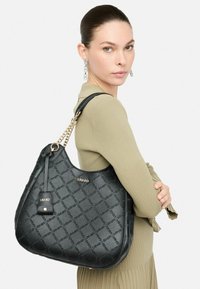 sac hobo noir en simili cuir texturé, présentant un motif en diamant et des accessoires en métal doré. Étiquette détachable avec logo de la marque. Accent en chaîne.
