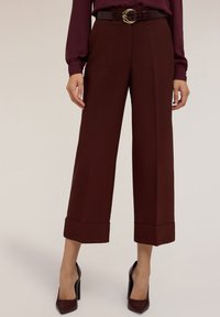 Bordeaux wijde broek met een getailleerde pasvorm, voorzien van een omgeslagen zoom en een gladde, textuurachtige afwerking. Draag met een bijpassende riem en hoge hakken.