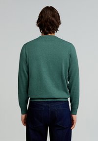 Grüner Strickpullover mit Rundhalsausschnitt, langen Ärmeln und glatter Textur, kombiniert mit dunkelblauen Jeans.