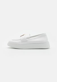 Scarpa slip-on in pelle bianca con una finitura liscia, suola rialzata, cuciture sottili e un accento dorato sulla tomaia.