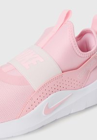 Ružové slip-on tenisky Nike s elastickým pásom, bielou podrážkou, perforovanou bočnou časťou a detailom "Just Do It" na pätnom púzdre.
