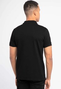 Čierne polo tričko s krátkymi rukávmi a klasickým golierom. Hladká textúra látky, jednoduchý design bez viditeľných vzorov alebo akcentov.