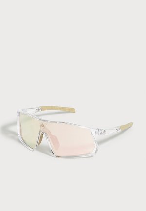 Lunettes de soleil à monture transparente avec de grandes verres rectangulaires légèrement teintés et des extrémités de branches beiges texturées sur un fond uni.