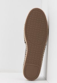 Semelle de chaussure en caoutchouc marron avec des motifs de bande de roulement présentant les initiales répétées "MK", sur un fond blanc en coin.