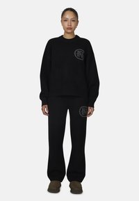 Zwarte gebreide trui met geribbelde manchetten, voorzien van een logo-patch, gecombineerd met bijpassende zwarte sweatpants met overeenkomende logo-accenten en een losse pasvorm.