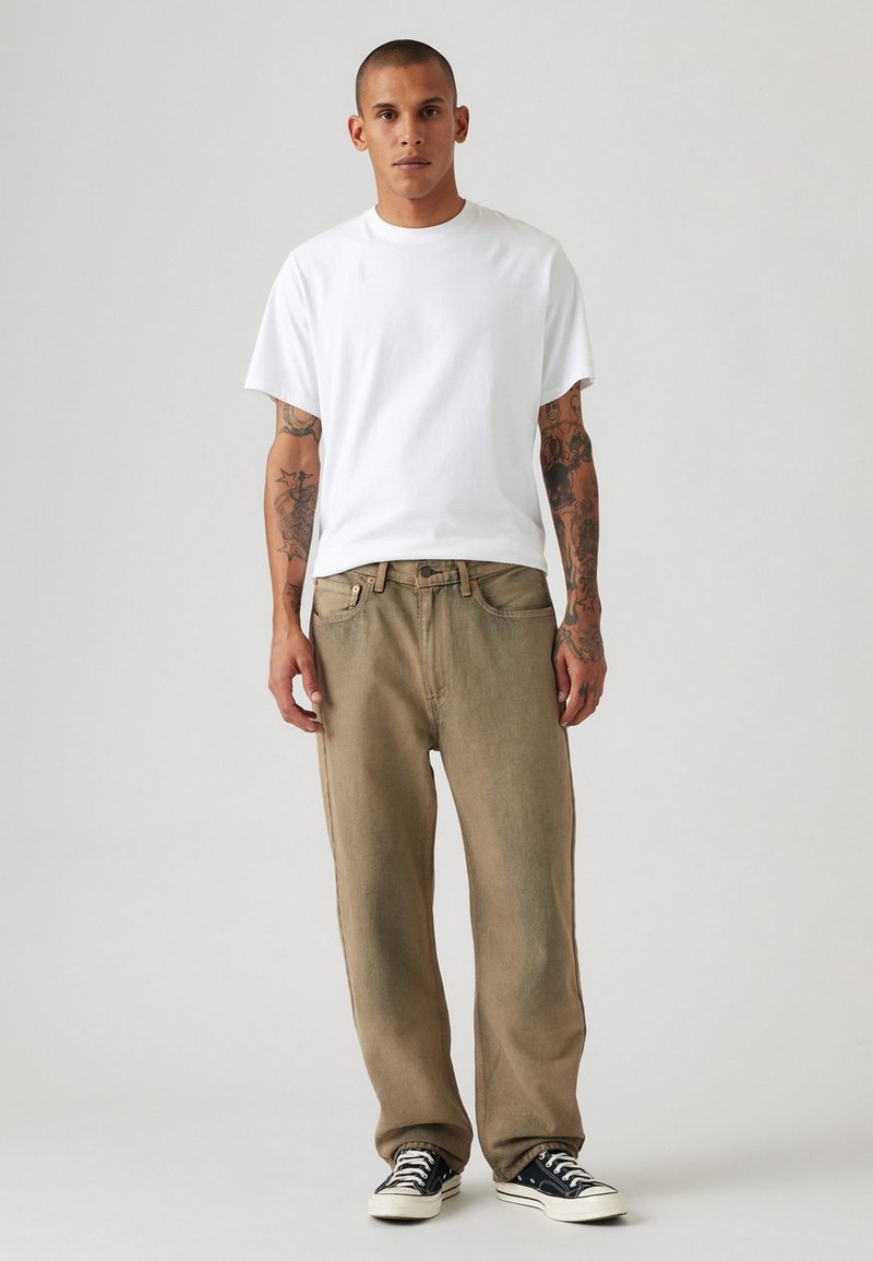 Camiseta blanca de manga corta combinada con jeans sueltos de color beige claro y zapatillas bajas en blanco y negro. Diseño simple y colores neutros.