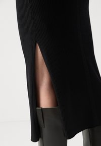Black ribbed skirt with side slit, featuring vertical textured lines. Accompanied by knee-high, flat black boots.