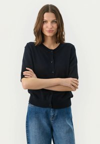 Jūras kara flotes īsajā piedurknē džemperis, apaļš kakls, priekšējā pogu aizdare, mīksta tekstūra, ribota apakšmala, apvienots ar gaiši ziliem džinsiem.