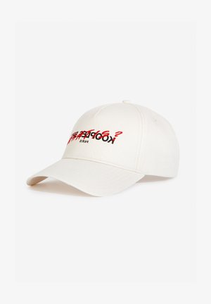 Casquette de baseball crème avec une visière incurvée, ornée de texte brodé rouge et noir. Fabriquée en coton, elle présente un design minimaliste sans motifs.