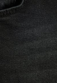 Tejido de mezclilla negra con una textura suave, ligeramente elástica y un cuello redondeado. Costuras visibles a lo largo de los bordes.