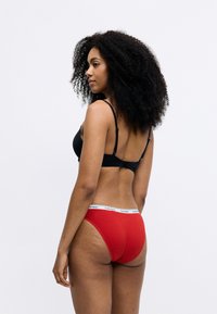 Fekete melltartó állítható pántokkal, piros pamut hipster alsónemű, fehér Calvin Klein derékszíjjal, sima felülettel és illeszkedő fazonnal.