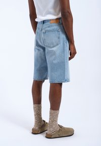 Lichtblauwe denimshorts met een ontspannen pasvorm, met achterzakken, gestikte zoom en een tan label op de tailleband. Gecombineerd met patroon sokken en klompen.