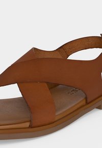 Καφέ δερμάτινο σανδάλι με φαρδιές σταυρωτές λουράκια και επίπεδη σόλα, σχεδιασμένο για καθημερινή χρήση και άνεση.