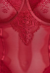 Body in pizzo rosso con tessuto trasparente. Presenta motivi floreali in pizzo intricati e bordi lisci. Tessuto morbido con un design aderente.