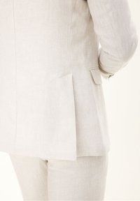 Světlý béžový lněný oblek s dobře padnoucím sakem a rozparky v slim-fit designu. Texturovaná tkanina se jemnými švy.
