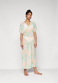Vestido largo y transparente con escote en V, mangas sueltas y un patrón abstracto en tonos pastel de verde menta y melocotón suave. La tela ligera cae con elegancia.